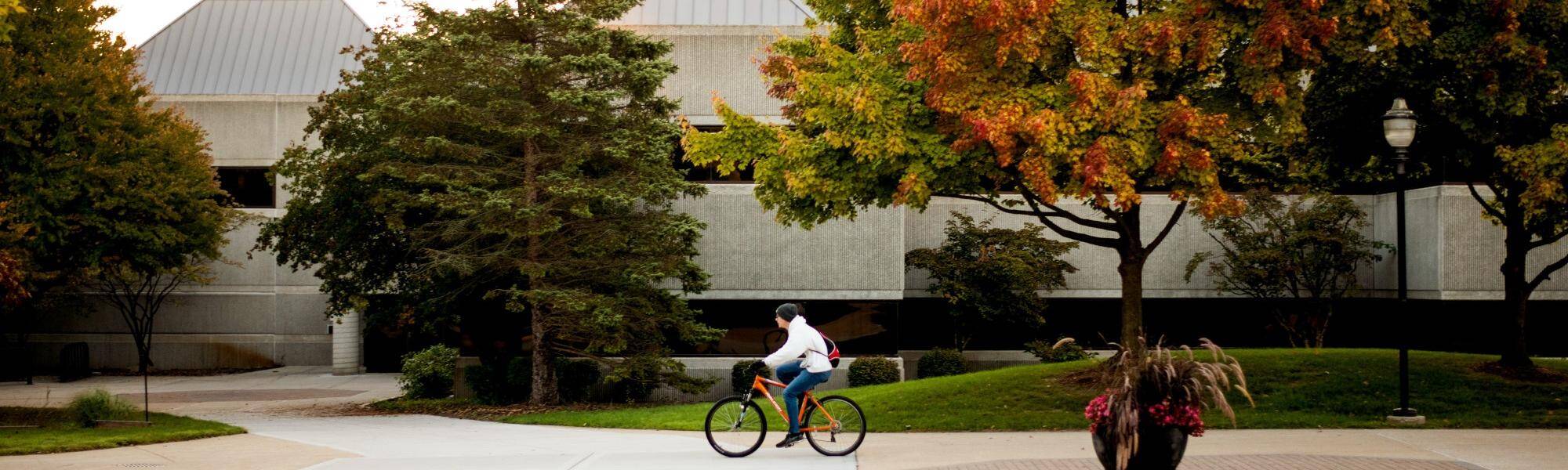 Front of Au Sable Hall in late summer or fall with someone riding bike in front of building